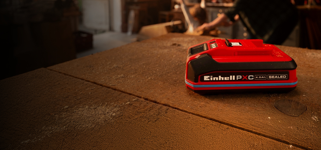 Einhell Power X-Change 4.0Ah SEALEAD battery on a wooden workbench, showing blue ring and label.