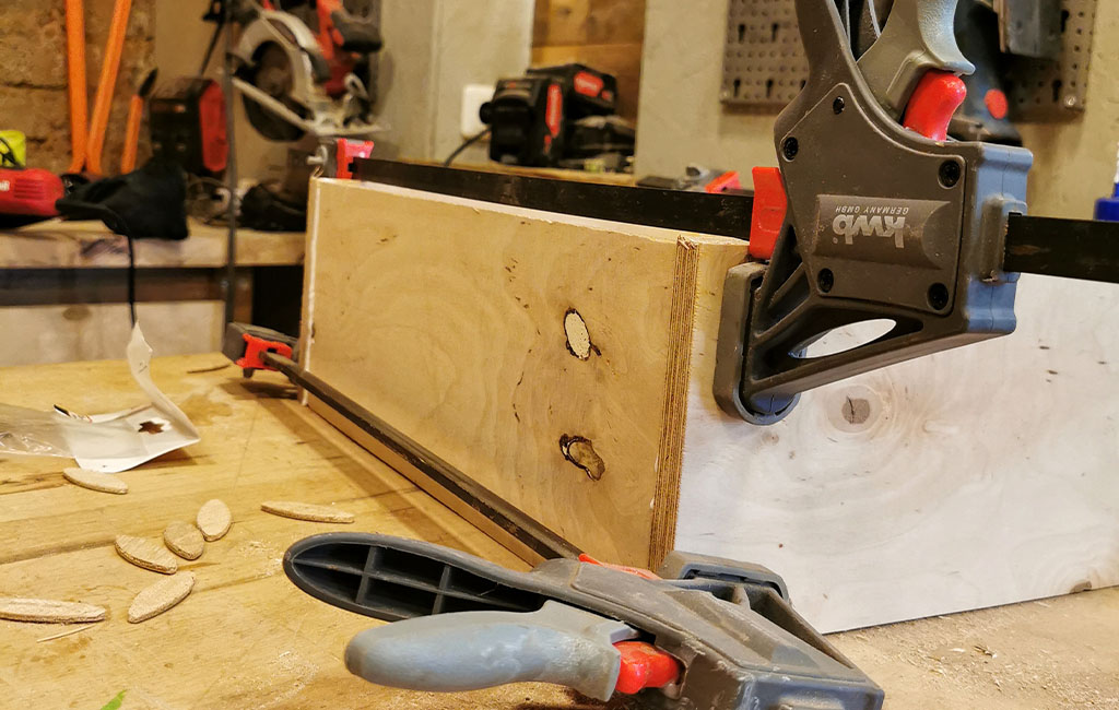 Two wooden boards clamped together with glue and clamps. Biscuit joiner pieces are scattered nearby.