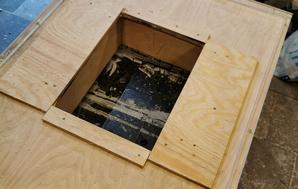 Close-up of a wooden board with a central square cut-out, secured with screws.