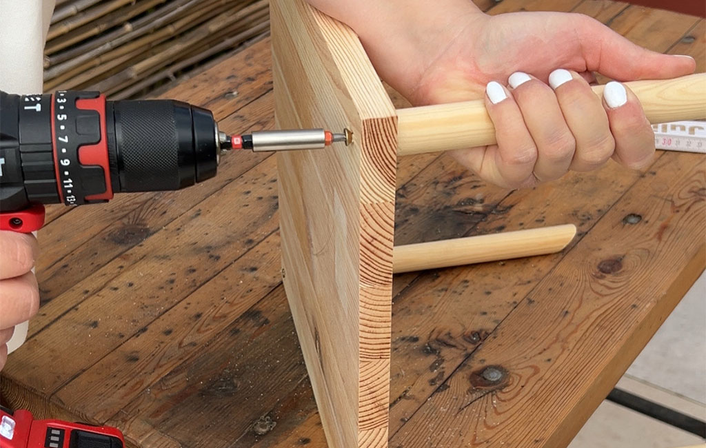 A person uses an Einhell cordless drill to screw wood pieces for building a bird feeder.