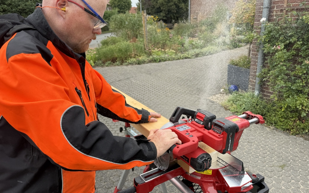 Eine Person in orange-schwarzer Arbeitskleidung bedient im Freien auf einem Ständer ein rotes Elektrowerkzeug.