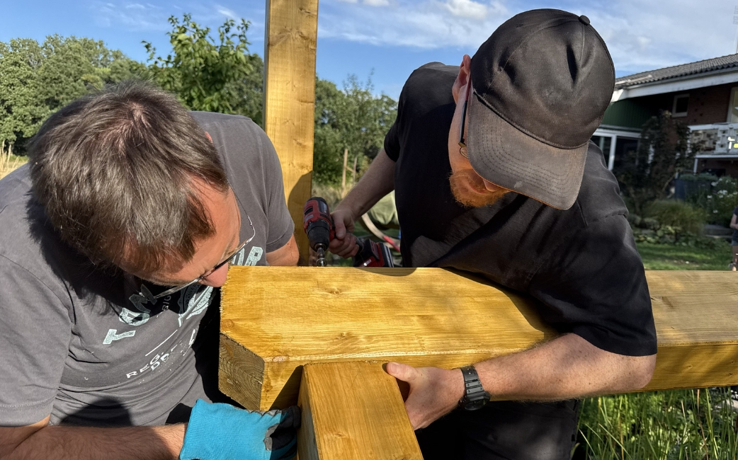 Zwei Personen montieren einen Holzbalken für eine Gartenpergola.