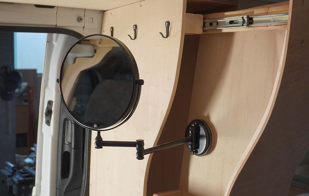 Swivel mirror with a telescopic arm mounted on a wooden wall inside a camper.