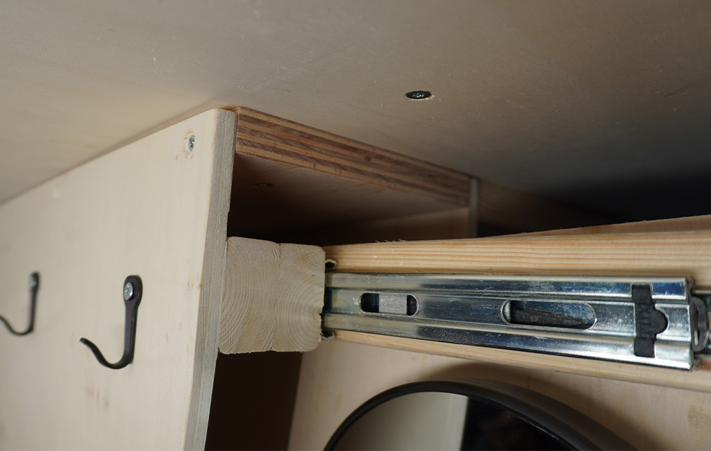 Close-up of a mounted metal drawer slide with wooden support inside a camper.