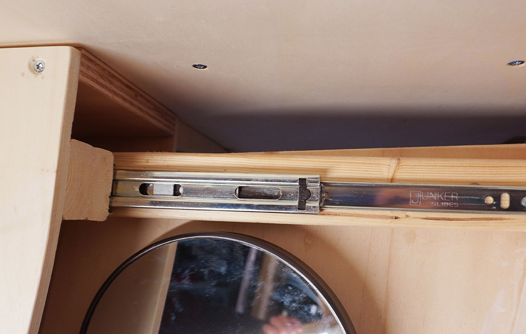 Metal drawer slide in camper with mirror below.
