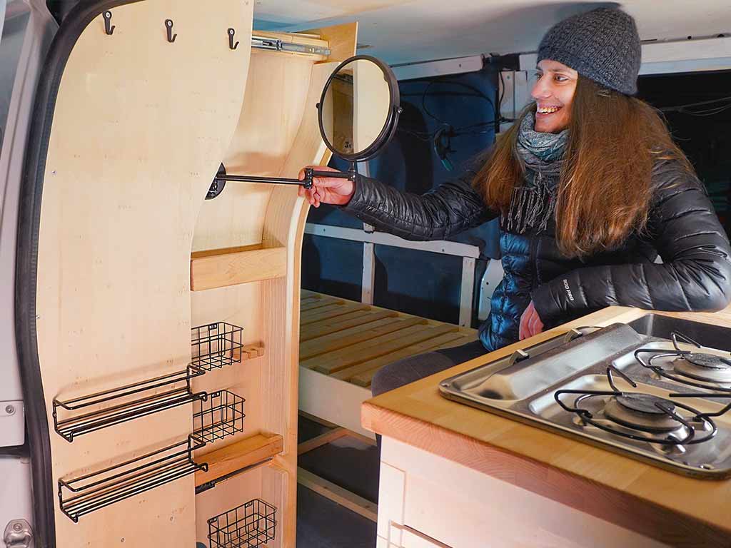 Woman sitting inside the camper smiling while pulling out the mirror from the bathroom cabinet.