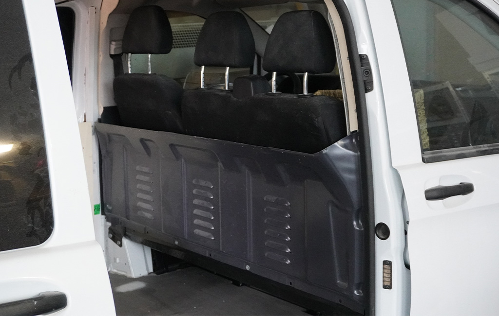 View into a van with black back seats and a black partition wall to the cargo area.