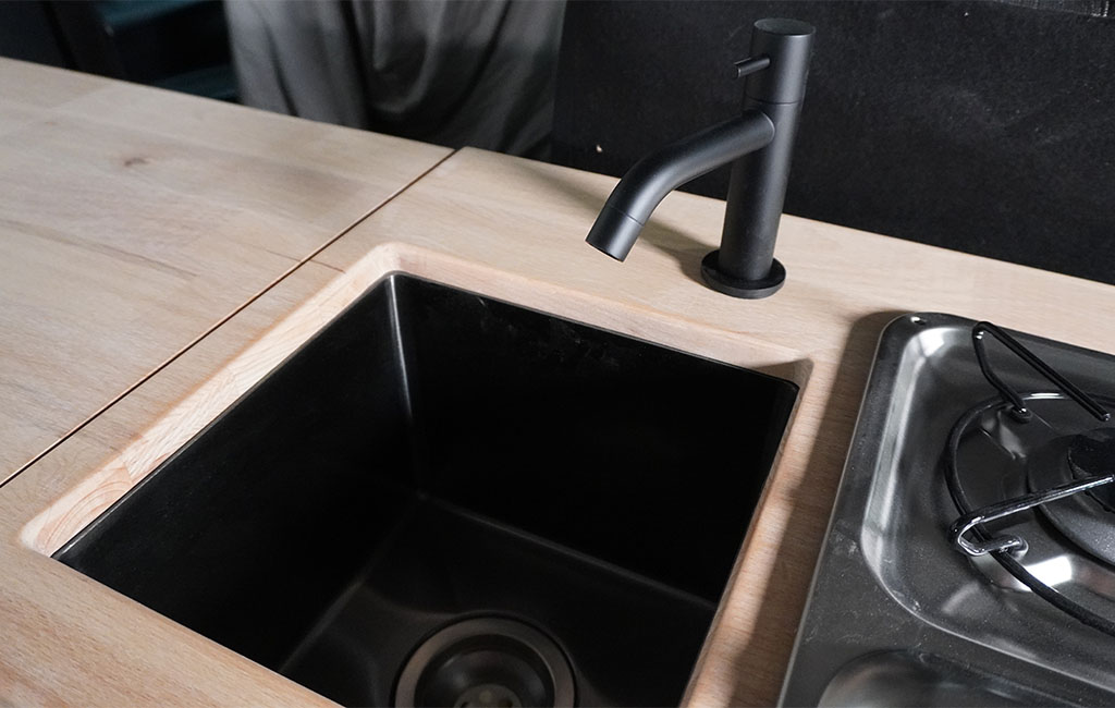 Close-up of a black sink and faucet in a wooden countertop next to a gas stove.