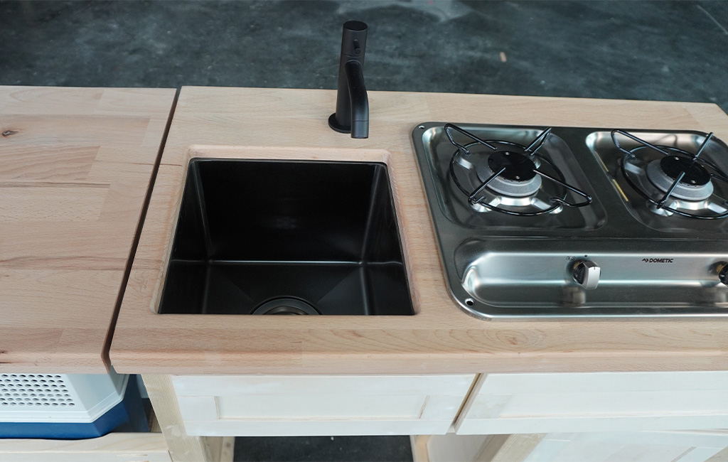 Black sink and a two-burner gas stove embedded in a light wooden countertop.