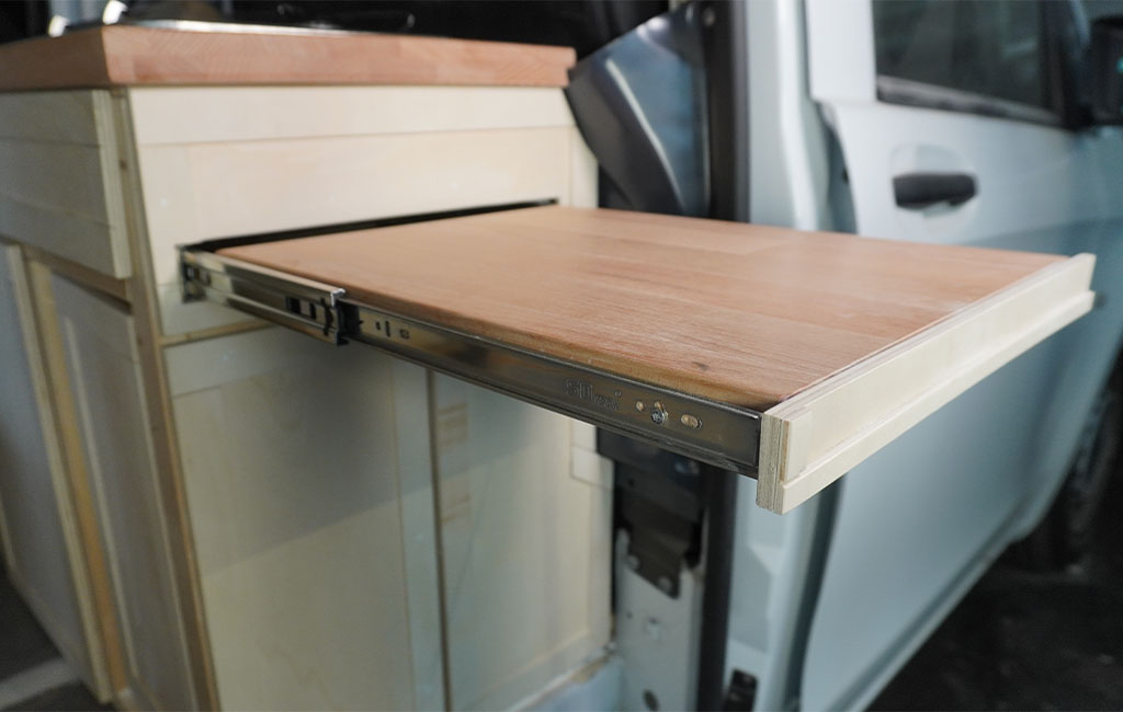 Extended wooden board on metal rails at the side of a kitchenette in the camper.