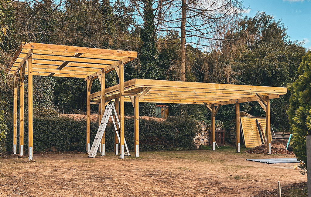 Two connected wooden carports under construction, a ladder stands in the middle.