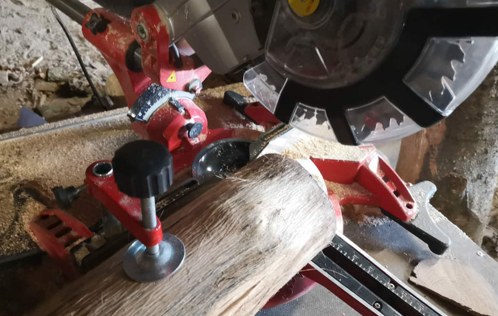 Cutting a wooden log with a miter saw as part of a DIY Christmas decoration project