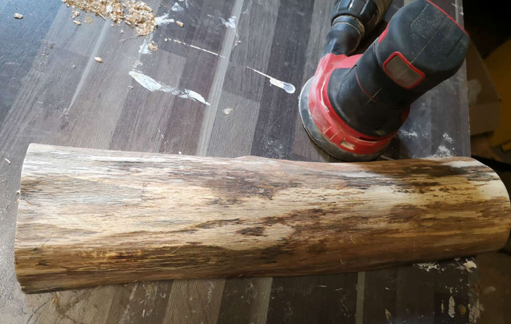 Sanding a wooden log to prepare it for a DIY decoration