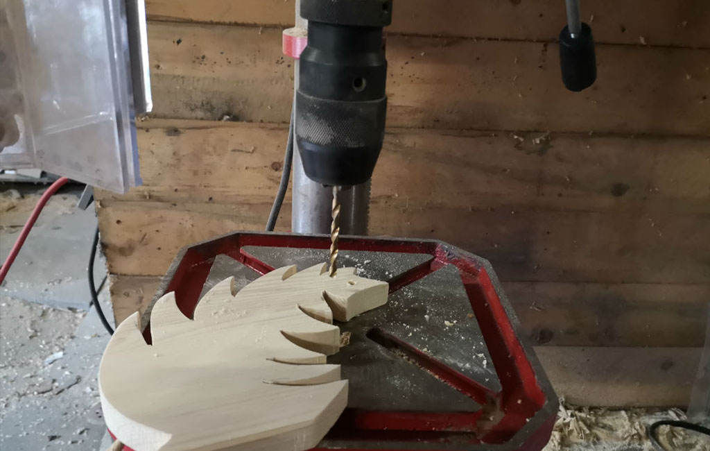 Using a drill press to make a hole in a wooden leaf cutout for a DIY Christmas decoration