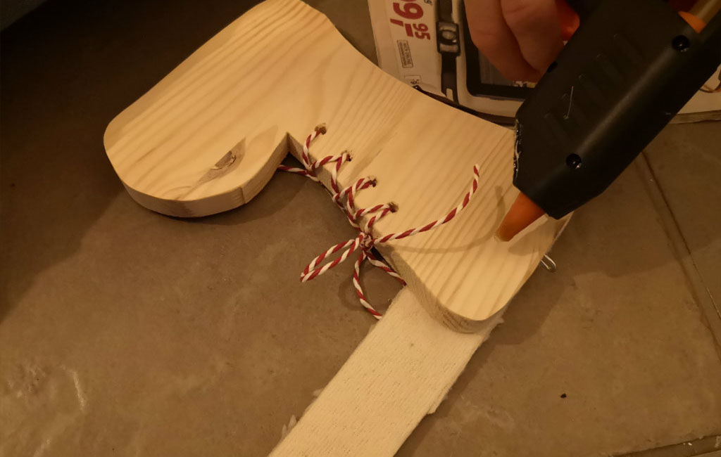 Using a hot glue gun to attach red-and-white twine to a wooden stocking for a DIY Christmas decoration