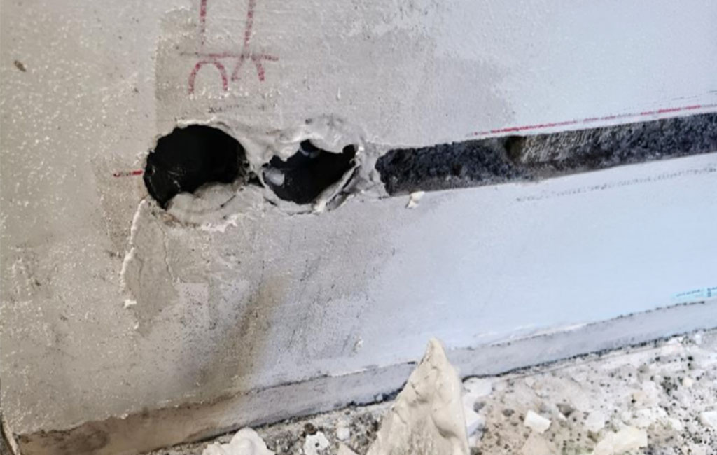 Two round drill holes and a slot in a wall, with dust and plaster debris below.