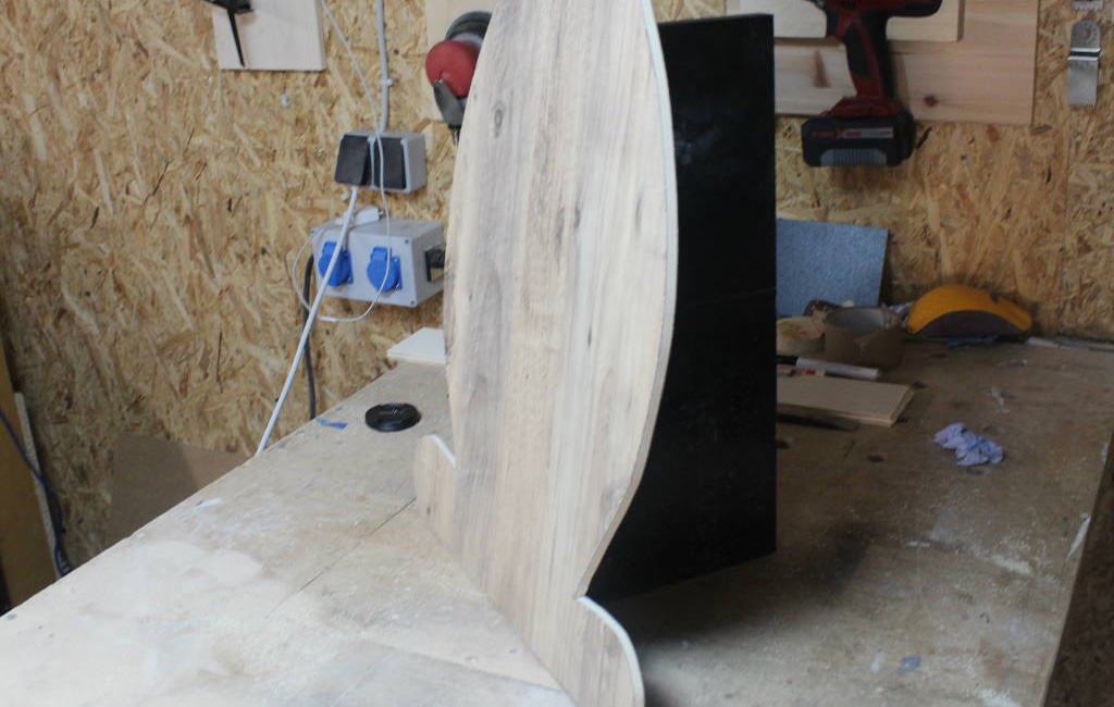 Cut-out wooden bunny stands upright with a black support in a workshop.