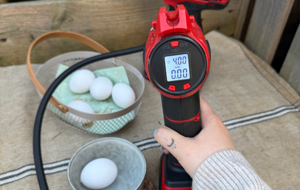 An Einhell cordless compressor with digital display is held next to eggs on a table.