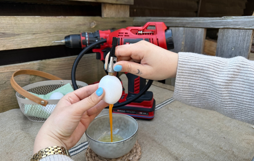 Air pressure is used to blow out an egg, yolk runs into a bowl, with an Einhell cordless compressor behind.