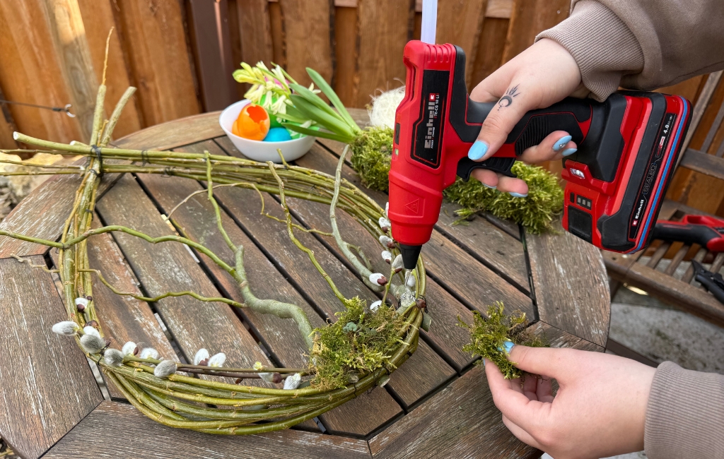 Einhell hot glue gun attaching moss to a wreath made of branches on a table.