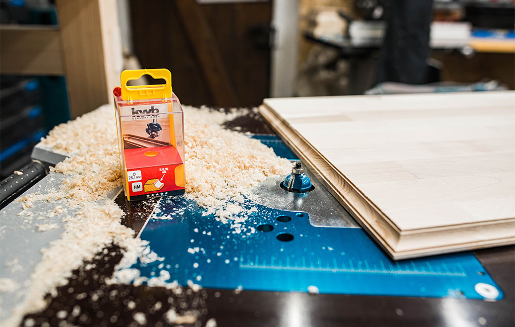 Router tool on a workbench, surrounded by wood shavings and milled wooden board.