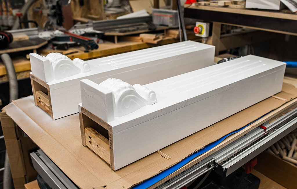 Two white-painted wooden supports with decorative details lie side by side on a workbench.