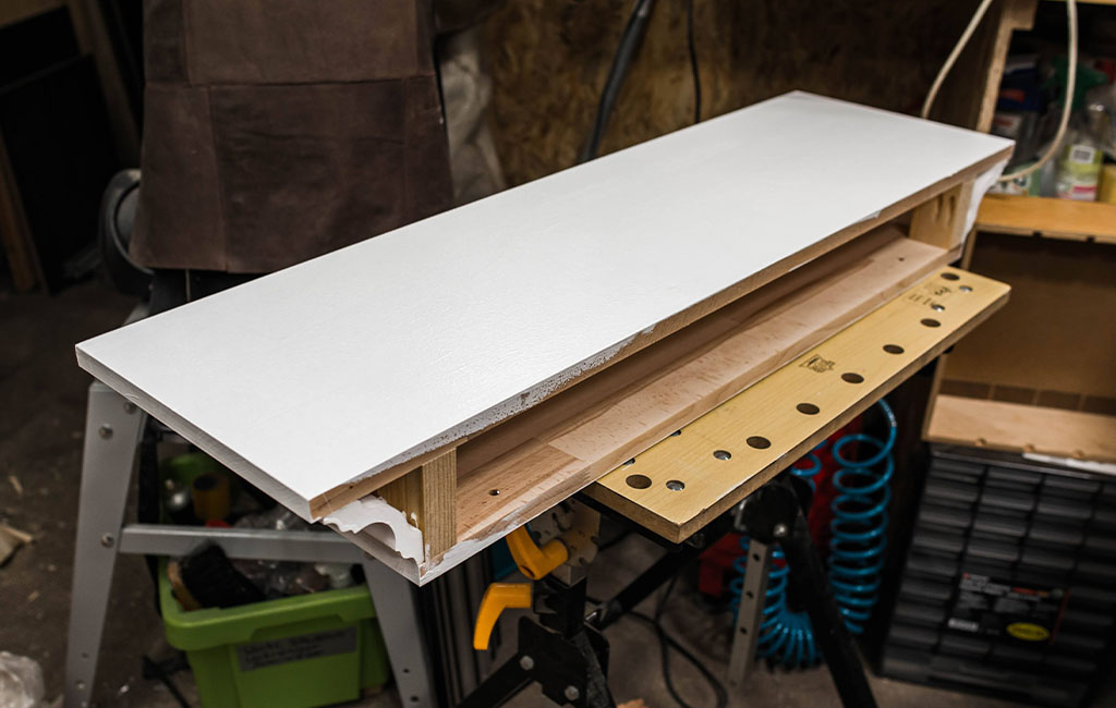 White-painted wooden fireplace mantel lying on its back on a workbench, inner structure visible.