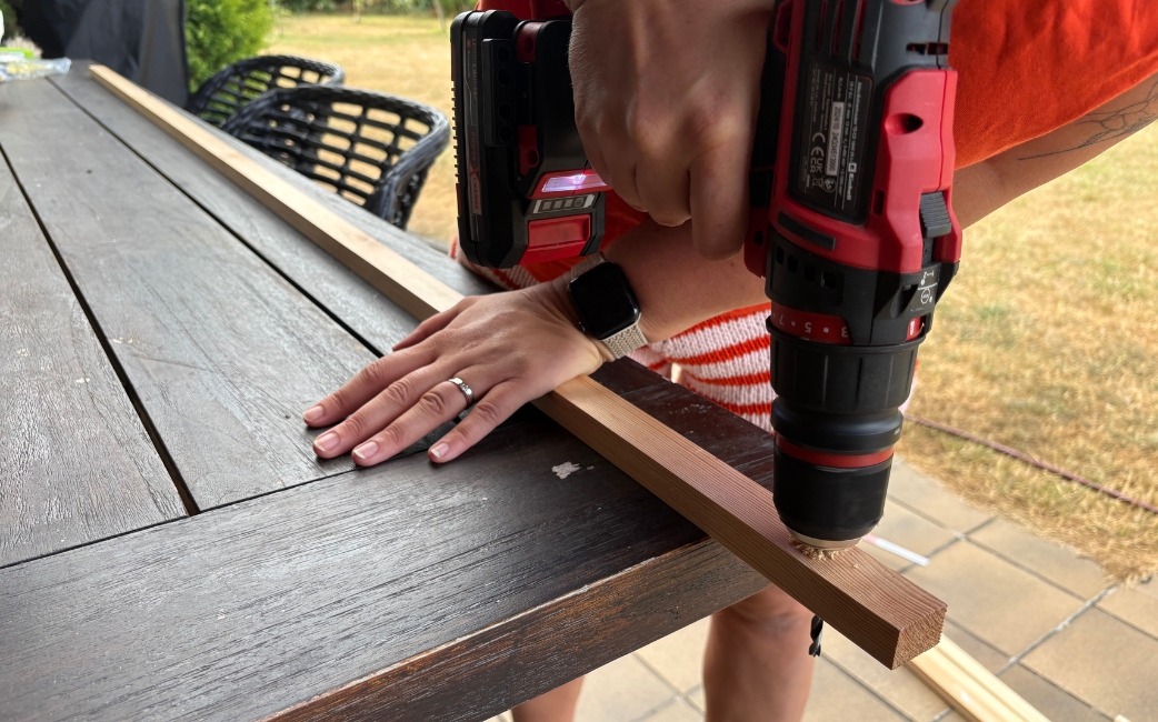 Close-up of a red Einhell cordless drill driver drilling a hole into a wooden strip.