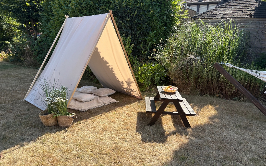 Beige Stoffbespannung über einem A-förmigen Holzgestell als Sonnenschutz im Garten, daneben Picknicktisch und Pflanzen.