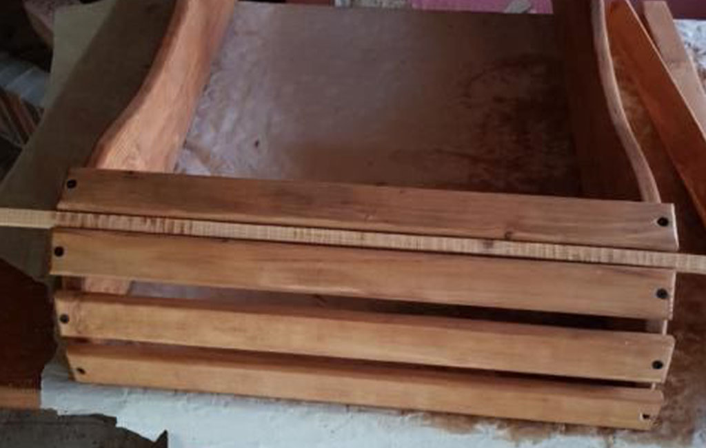 Der Rahmen eines Holz-Gartenstuhls liegt auf einer Werkbank, mehrere Querlatten sind montiert.