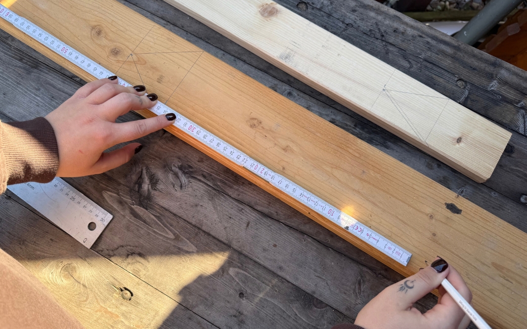 Eine Person misst ein Holzbrett mit einem Zollstock ab und markiert es mit einem Bleistift.