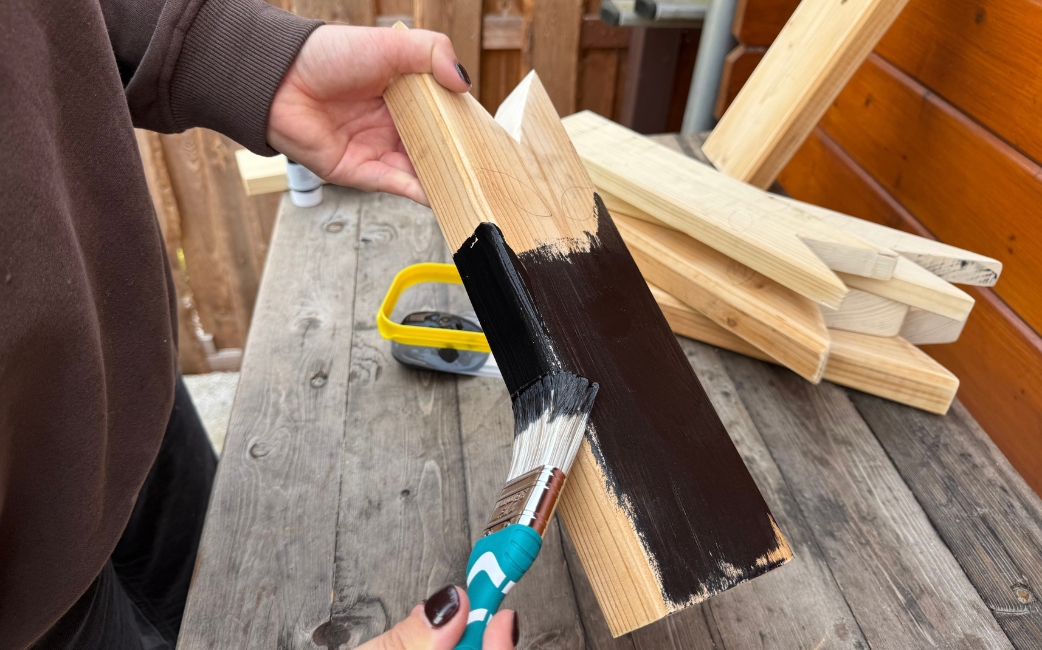 Jemand streicht ein zugeschnittenes Holzbrett mit schwarzer Farbe an.