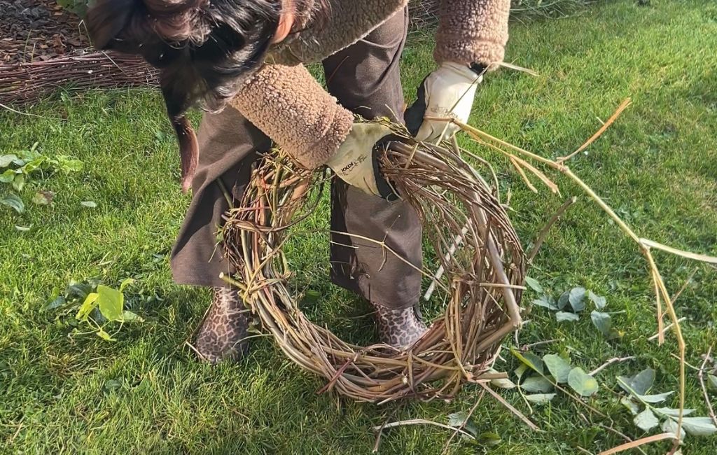 A person shapes a wreath from flexible branches on the lawn.
