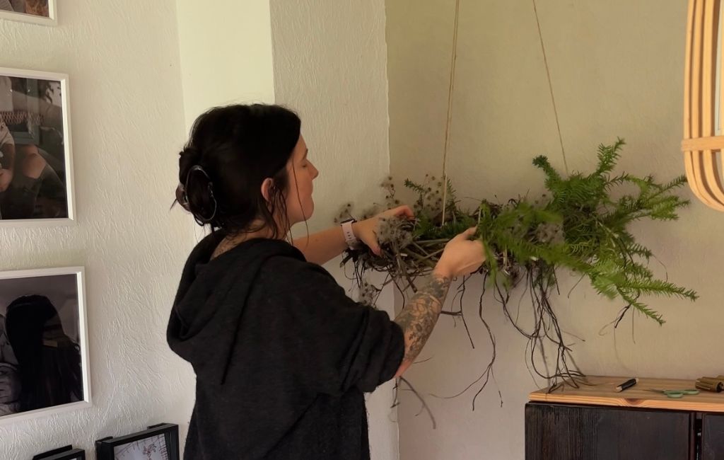 A woman decorates the hanging Advent wreath with green branches and natural materials.