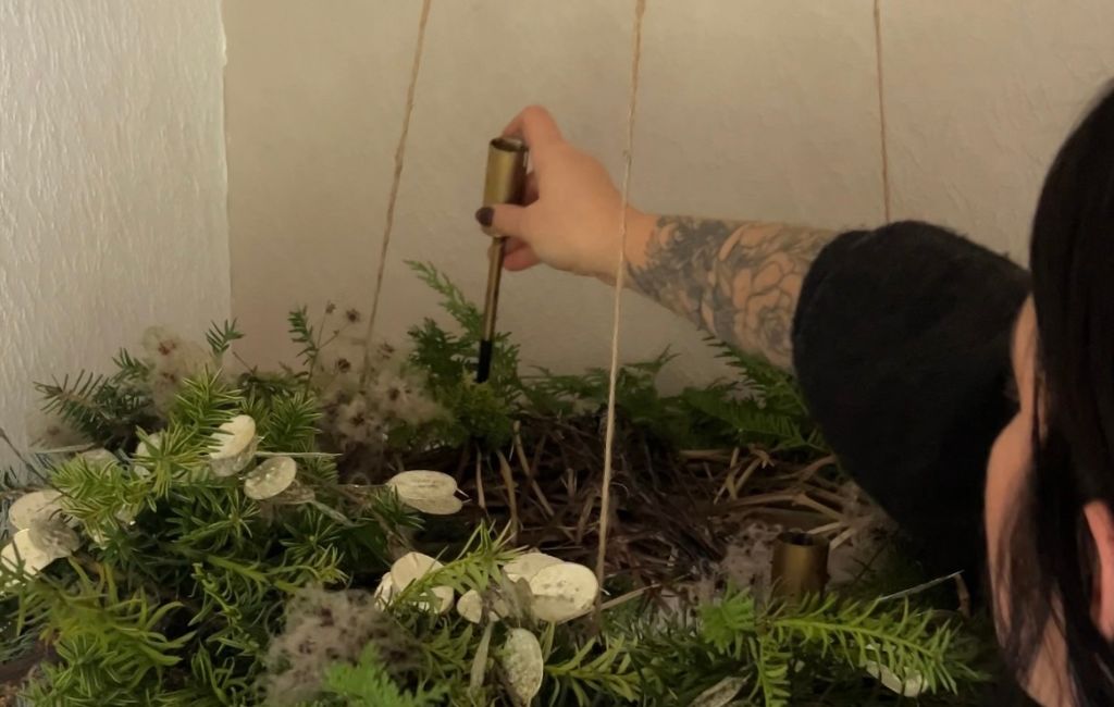 A hand inserts a brown candle into a gold-coloured holder in the Advent wreath.