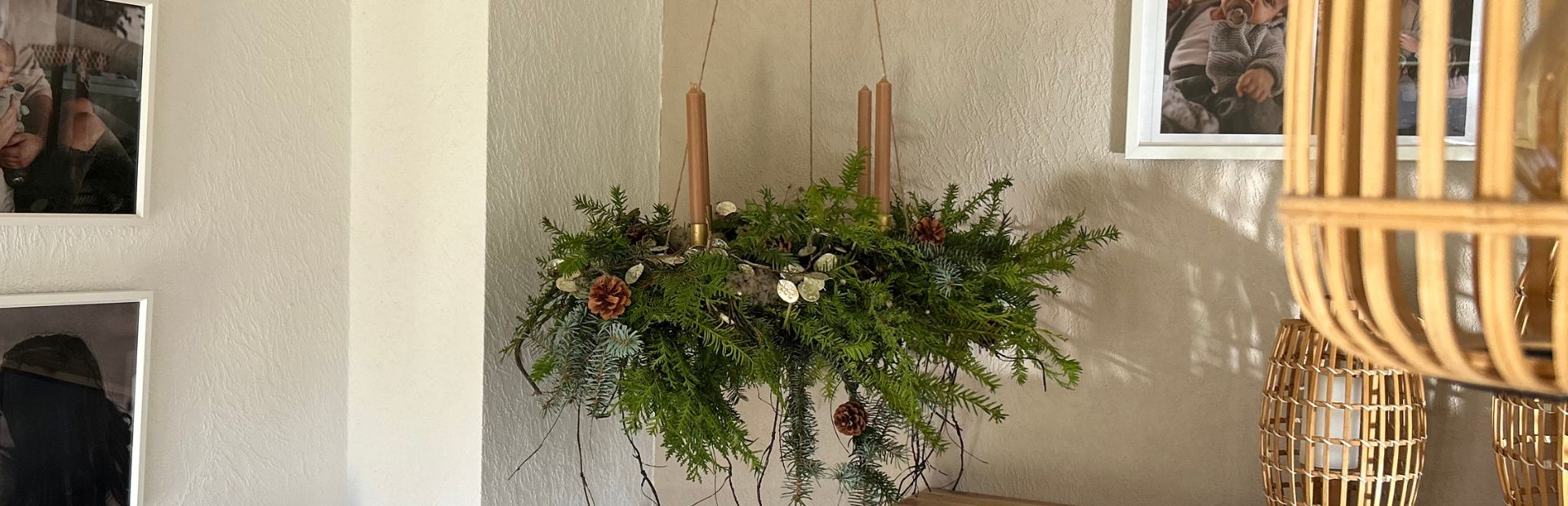 A hanging Advent wreath made of fir greenery with four brown taper candles, decorated with cones and dried plants.