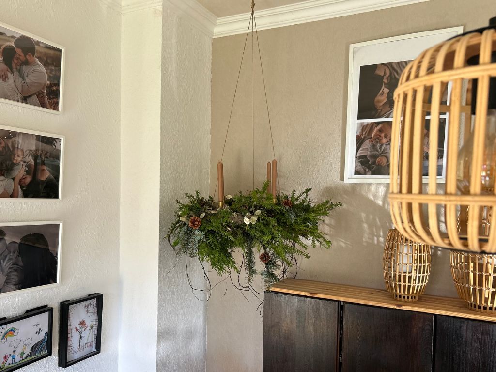 A hanging Advent wreath made of fir greenery with four brown taper candles, decorated with cones and dried plants.