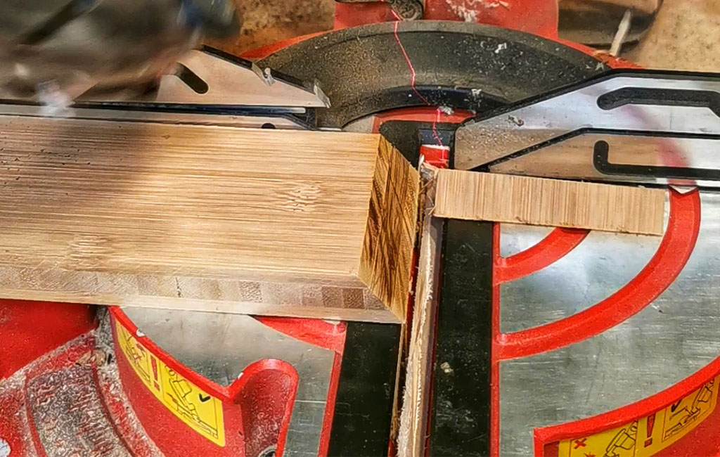 A miter saw cuts a piece of wood precisely on a red saw table.