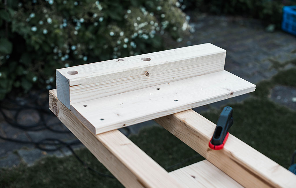 Wooden beams with drill holes clamped together on a workbench.