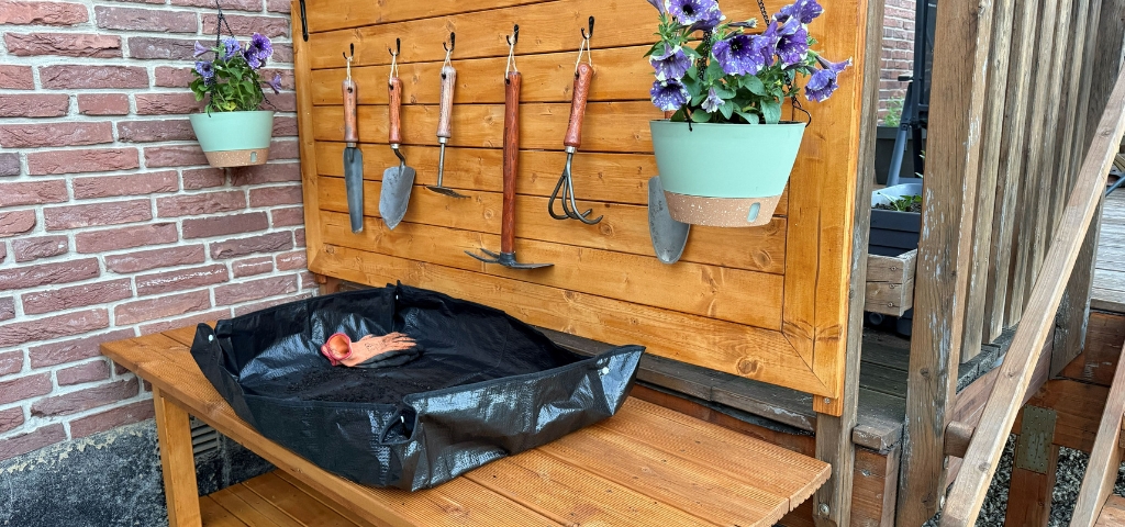 Ein fertig dekorierter Pflanztisch mit Rückwand, Gartenwerkzeugen, Blumenampel und Pflanzunterlage.