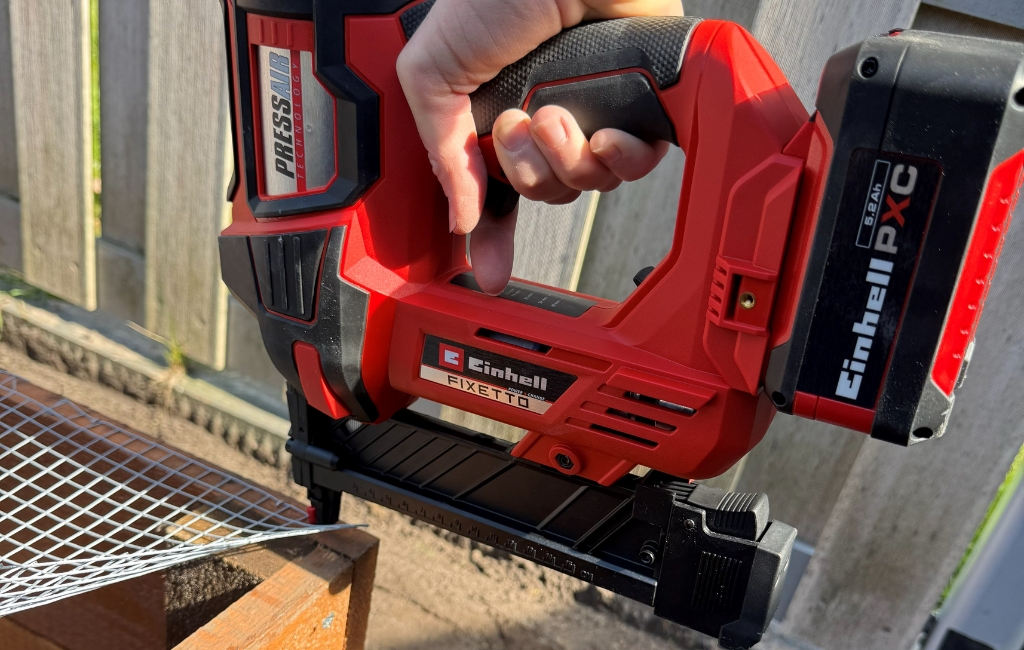 Nahaufnahme des Einhell Akku-Naglers FIXETTO, der ein engmaschiges Drahtgitter an einem Holzbalken befestigt.