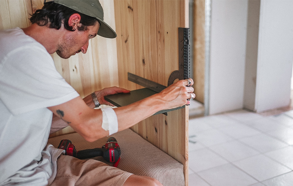 Ein Mann misst mit einem Winkel die Position einer Ablage im Strandkorb aus Holz aus.