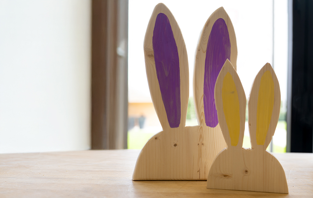 Two finished wooden rabbits with purple and yellow painted ears stand on a table.