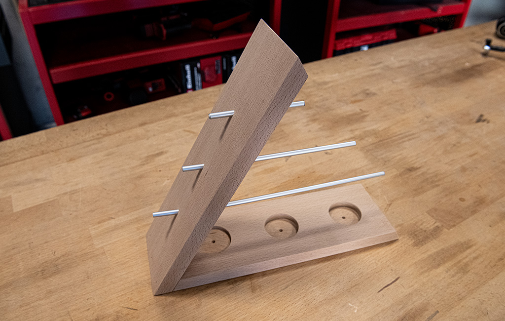 A slanted wooden jewellery stand with four inserted metal rods and three round cut-outs in the base.