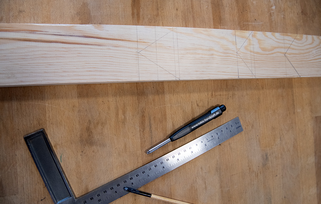 A long wooden board with outlined shapes of small houses, next to a ruler, pencil, and square.