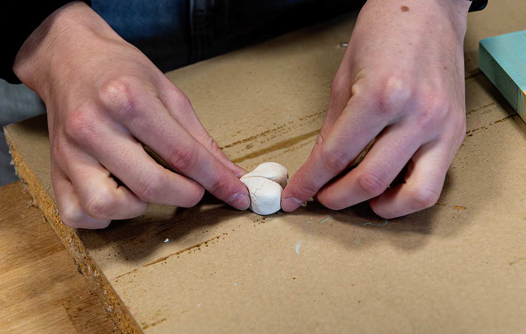 Two hands are shaping a small heart from white modeling clay.