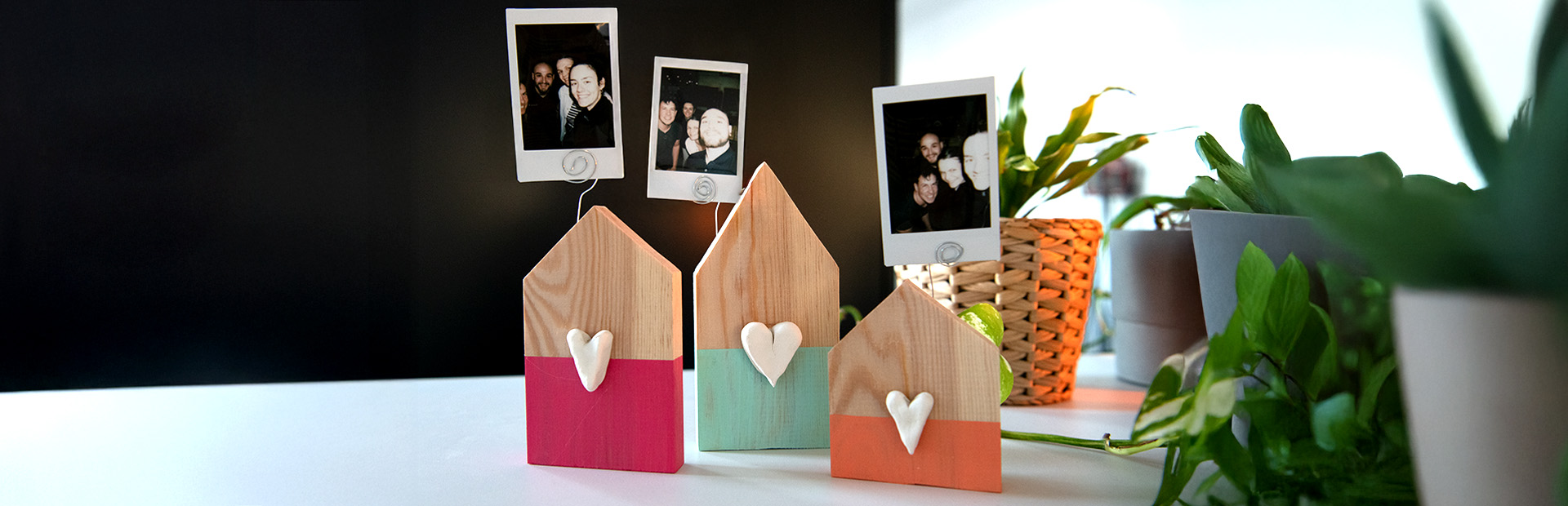 Three decorated wooden photo holders with instant photos stand among houseplants.