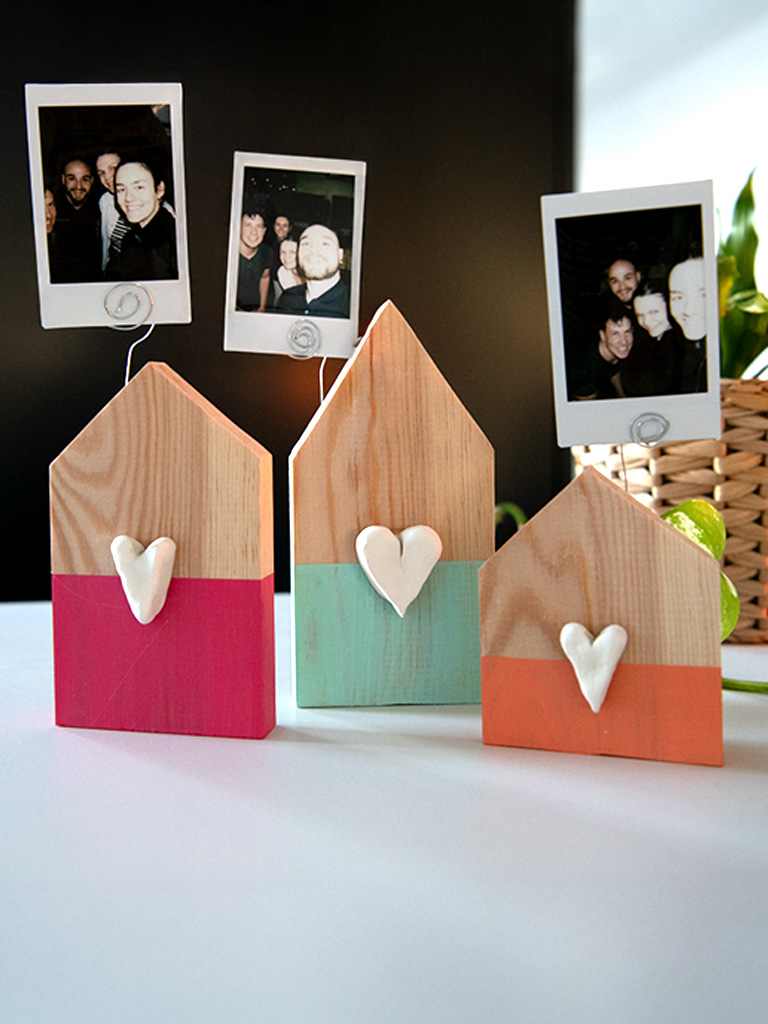 Three decorated wooden photo holders with instant photos stand among houseplants.
