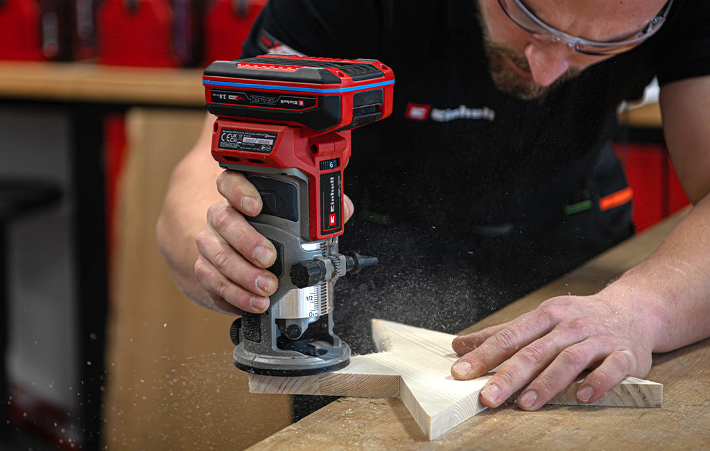 Eine Person fräst mit einer Kantenfräse die Kanten eines Holzsterns; Holzstaub ist sichtbar.