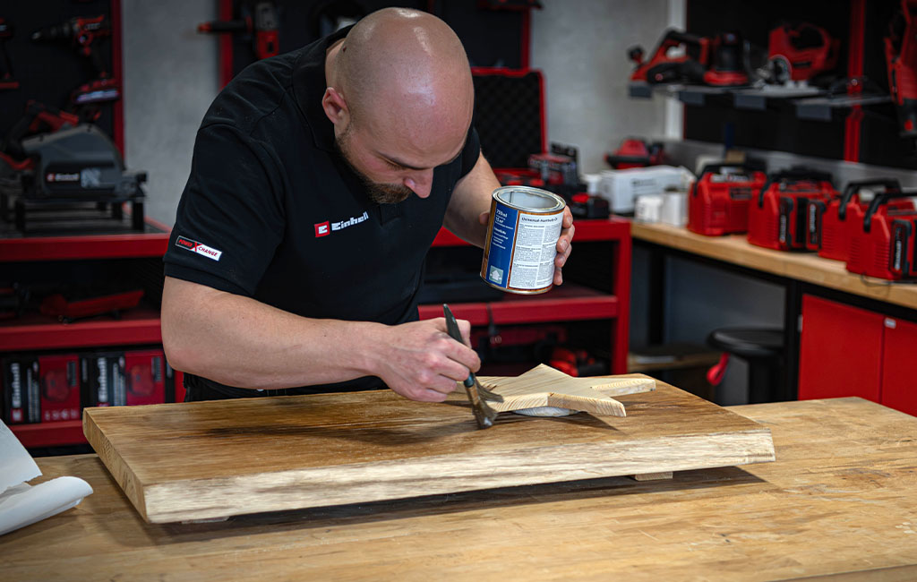 Eine Person streicht mit einem Pinsel Holzöl auf eine Holzplatte und einen Stern aus Holz.